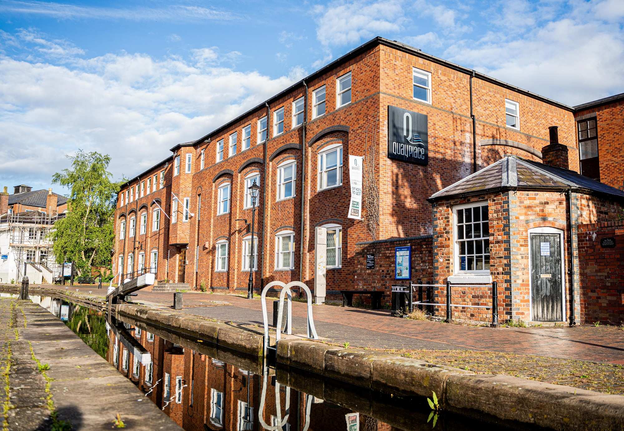 A big square building made from red brick in the style of the industrial revolution overlooking a canal.