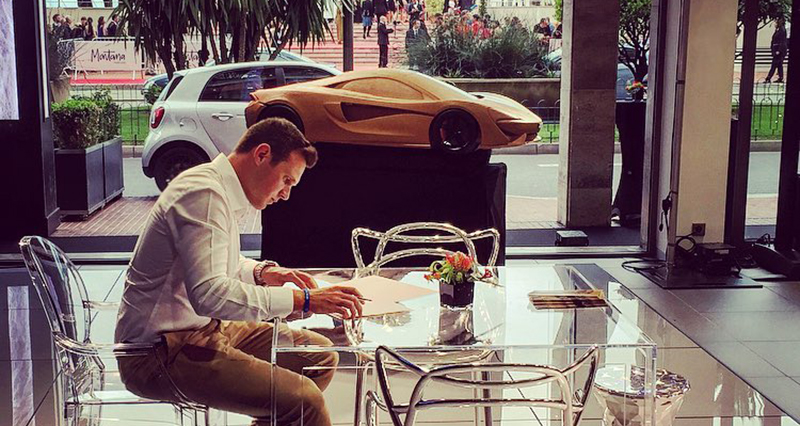 一个人坐在桌子前，面前放着文件;背景中可以看到一辆跑车的模型。