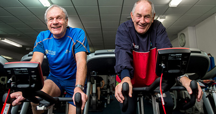 两个上了年纪的男人在健身自行车上咧着嘴笑。