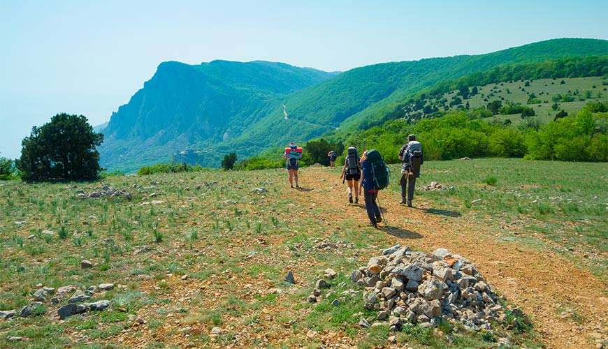 Hikers cross a plateau in a sunny, mountainous landscape.