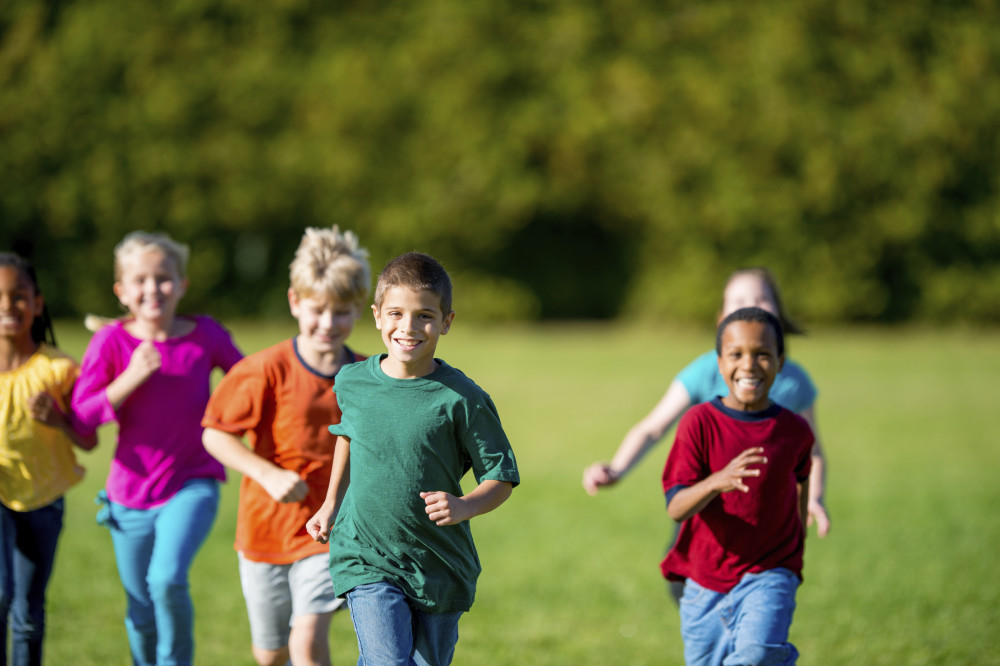 Children running across a grassy field on a sunny day.