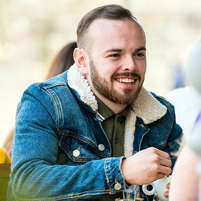A male student wearing a denim jacket and smiling at a coffee shop.