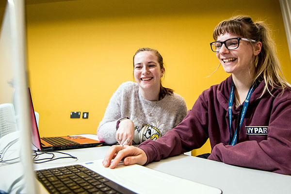 Two students smiling and looking at laptop