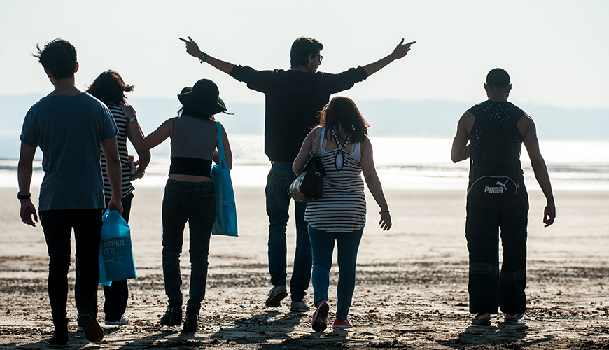 海滩上的学生离开镜头走向大海，领头的学生热情地展开双臂。