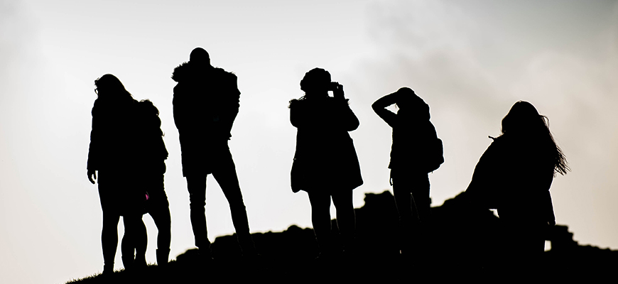 The black silhouettes of students stand on a ridge with a misty grey sky in the background.