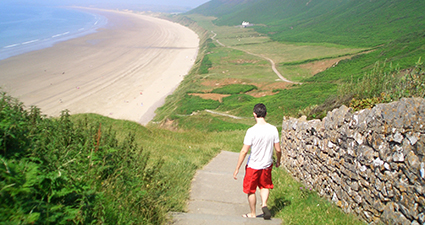一个年轻人沿着山坡上的小路走向一大片海滩。