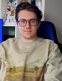 Liam Radcliffe wearing glasses and a beige jumper leans back in an office chair.
