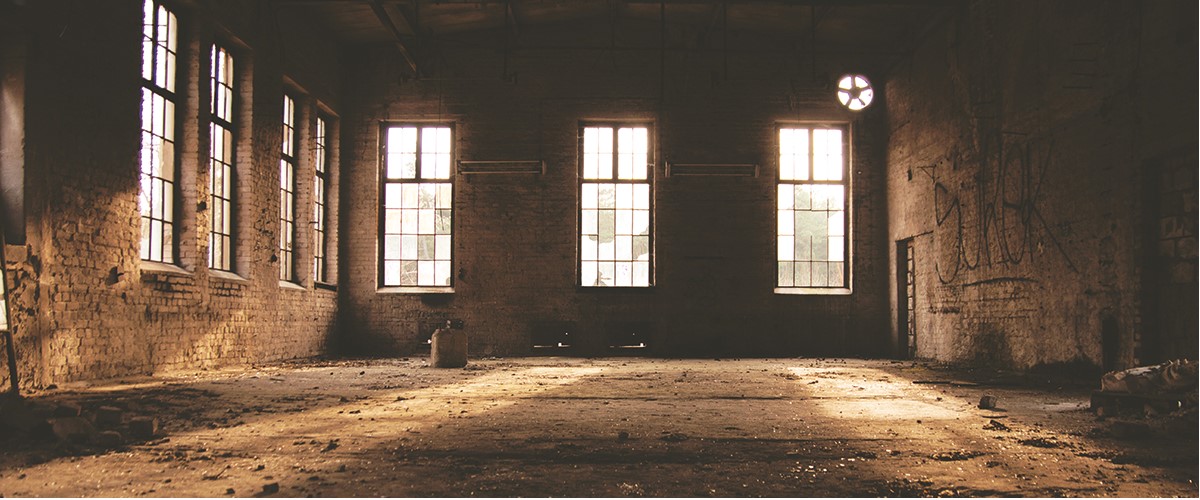 一个砖砌仓库阴暗的内部;从三扇大窗户透进来的光线穿过肮脏的地板。