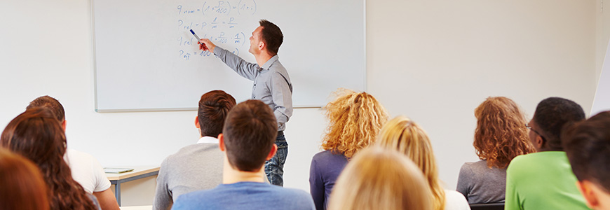 A teacher pointing at a whiteboard in front of his class.