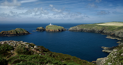 一座白色的小灯塔坐落在平静的蓝色海湾中的一座岩石岛上。